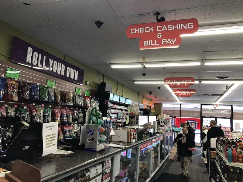 This view down our main aisle shows customers browsing wine near the Check Cashing & Bill Pay station, right where roll-your-own tobacco and cigars are also within reach. It's a snapshot of how our store blends everyday retail with essential financial services under one roof. Customers browsing the wine aisle near the Check Cashing and Bill Pay counter at GS Vape in Barberton, Ohio.