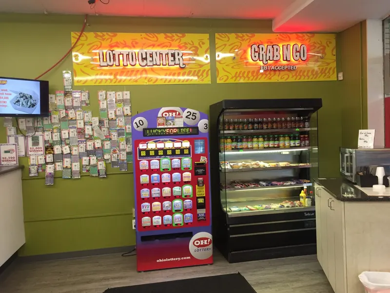 Our Lotto Center wall is stocked with Ohio Lottery scratch-offs and a slot machine ticket dispenser for players chasing the next big win. Right next to it, our Grab N Go cooler keeps fresh drinks and snacks within easy reach, and yes, EBT is accepted here too. Lotto Center and Grab N Go signage above a scratch-off ticket display and grab-and-go food cooler at GS Vape in Barberton, Ohio.