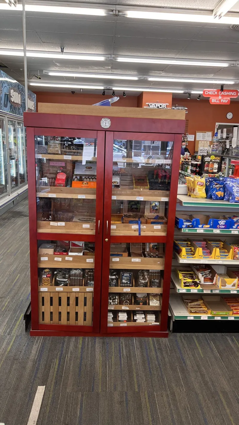Our humidified cigar cabinet keeps premium cigars fresh and ready, with everything organized by brand and box size behind glass doors. It sits right near our Check Cashing & Bill Pay counter, so you can grab a cigar while you handle your financial errands. Full view of the walk-in style cigar humidor cabinet with cigar boxes near the check cashing sign at GS Vape in Barberton, Ohio