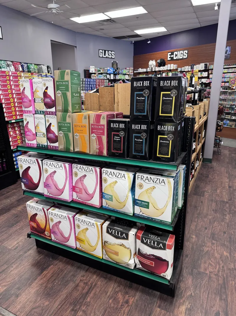 GS Vape Madison stocks a full boxed wine display with Franzia, Black Box, Bota Box, and Vella options for larger gatherings. The E-Cigs section is visible just behind the display for customers shopping multiple categories. Boxed wine selection display featuring Franzia and Black Box at GS Vape in Madison, Ohio