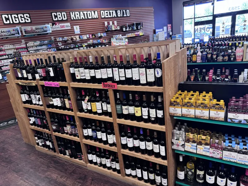 This wooden wine rack at GS Vape Madison organizes red wines by varietal, including Zinfandel, Syrah, and Bordeaux sections. It sits near the CBD, kratom, and Delta 8 wall for easy navigation of the store. Red wine rack organized by Zinfandel, Syrah, and Bordeaux varietals at GS Vape in Madison, Ohio